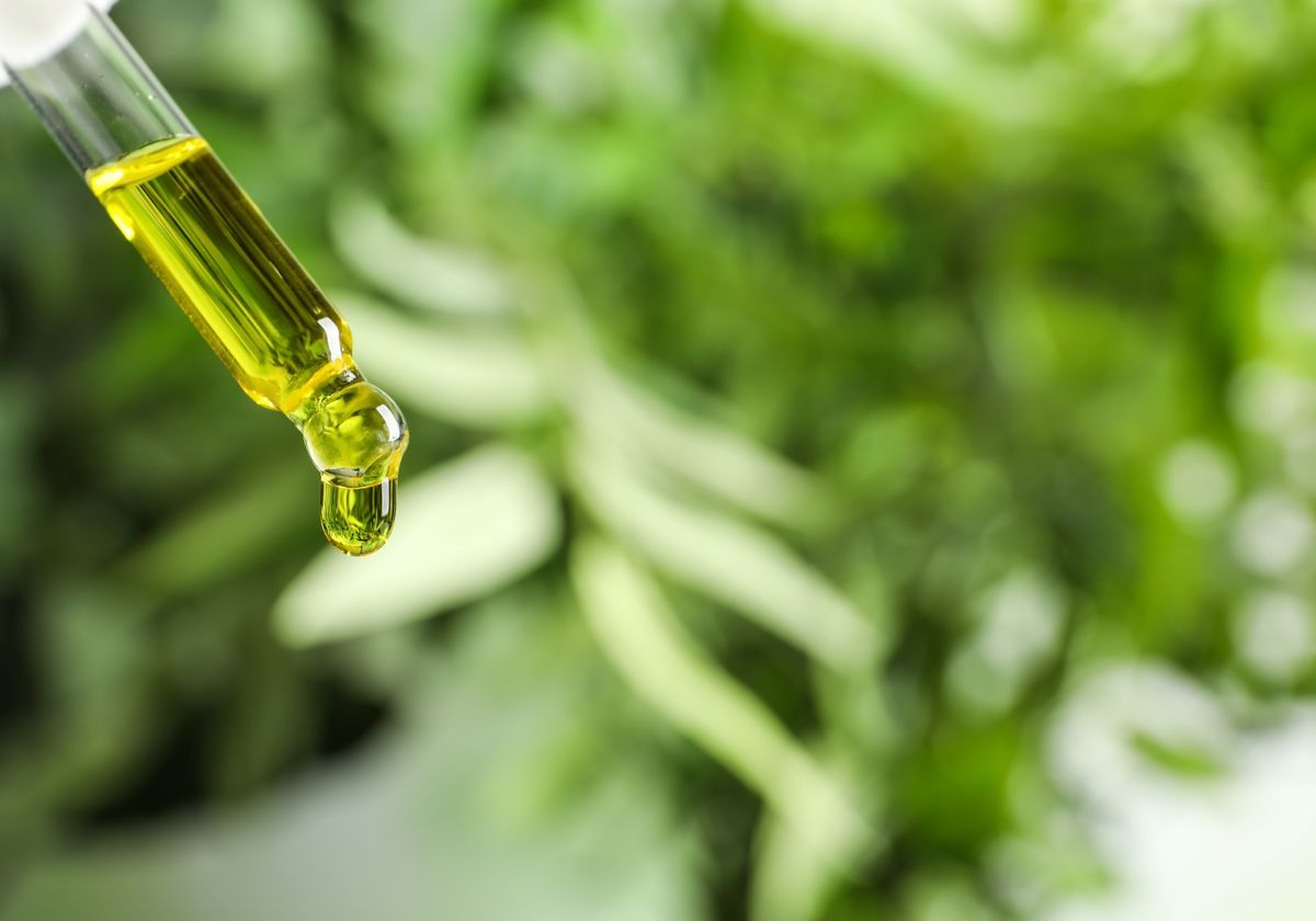 A pipette releasing oil over fresh green herbs
