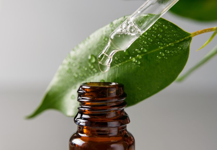 A dropper over a bottle of essential oil beside a green leaf